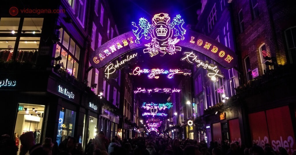 A Carnaby Street enfeitada na época em que o filme Bohemian Rhapsody saiu. É noite e a rua está lotada de pessoas.