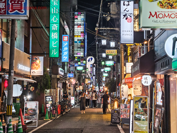 A foto mostra uma rua iluminada por letreiros, com restaurantes, na região de Umeda.