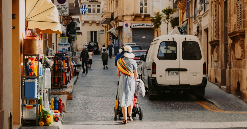 Mulher passeia com carrinho de bebê ao lado dos carros em cidade da Ilha de Malta. 