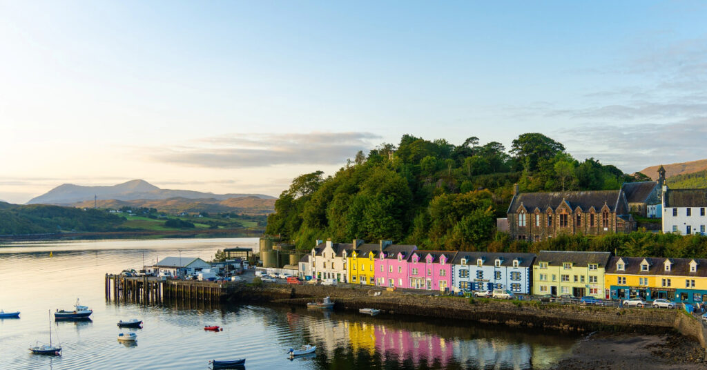 A imagem mostra as casinhas coloridas da baía de Portree, na Ilha de Skye, parte da Escócia. 