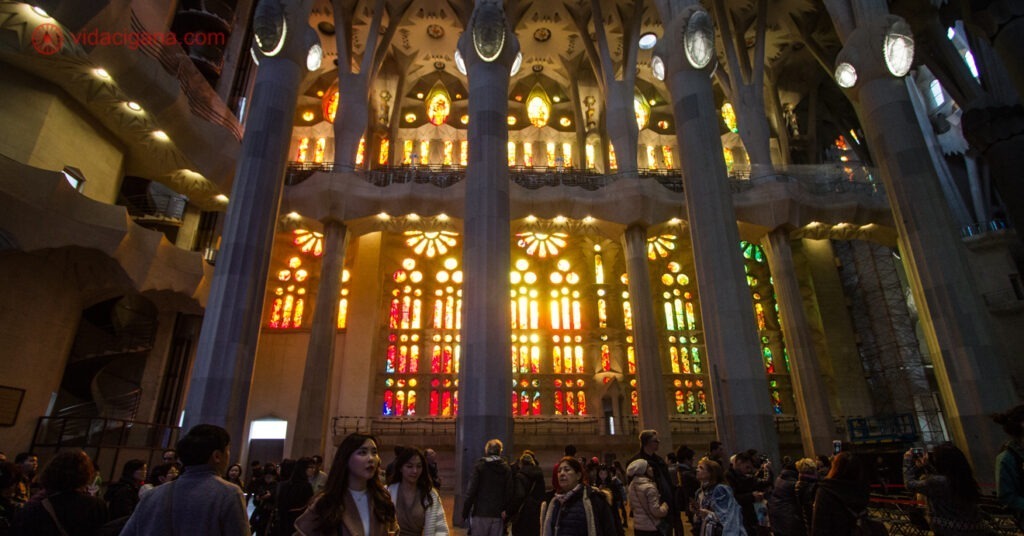 O interior da Sagrada Família. Na imagem estão os vitrais e muitos turistas. 