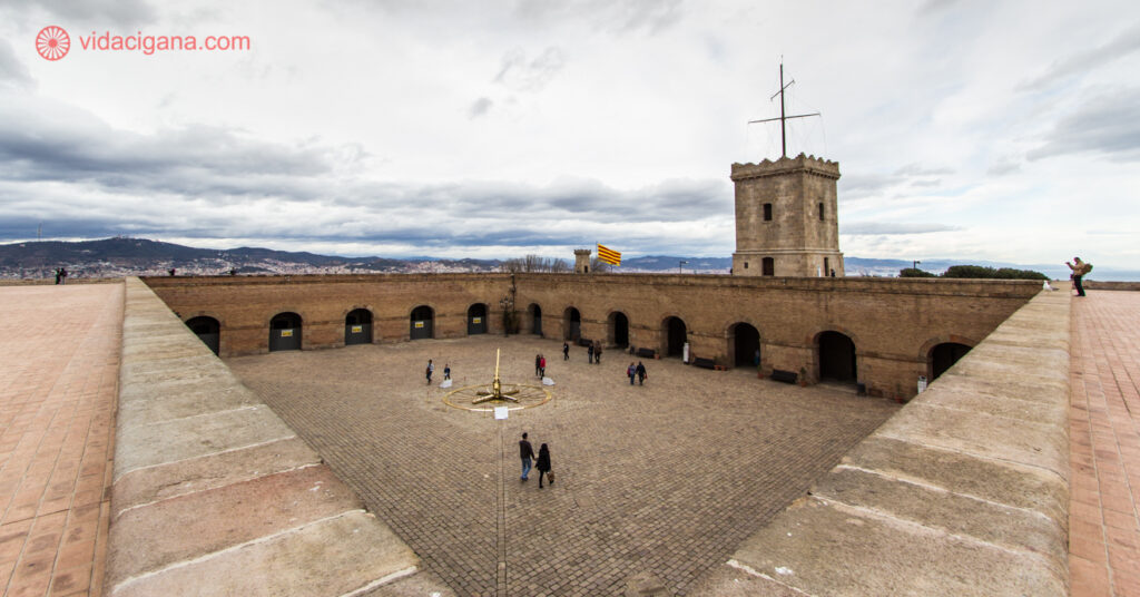 A vista do topo do Castelo de Montjuïc, com pessoas andando no átrio, entre as paredes da torre