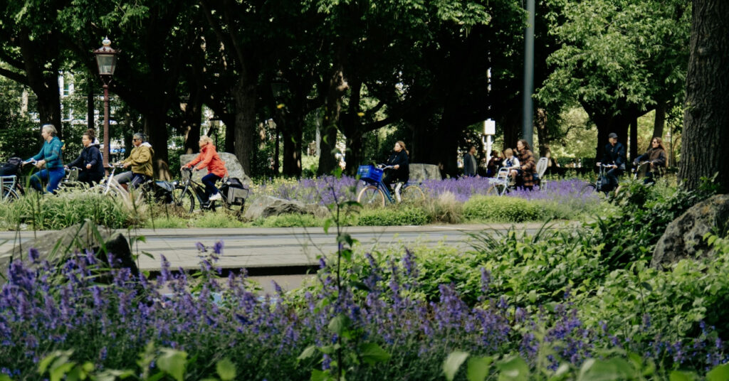 A imagem mostra pessoas passeando de bicicleta em um parque de Amsterdam, uma atividade muito comum na cidade. 