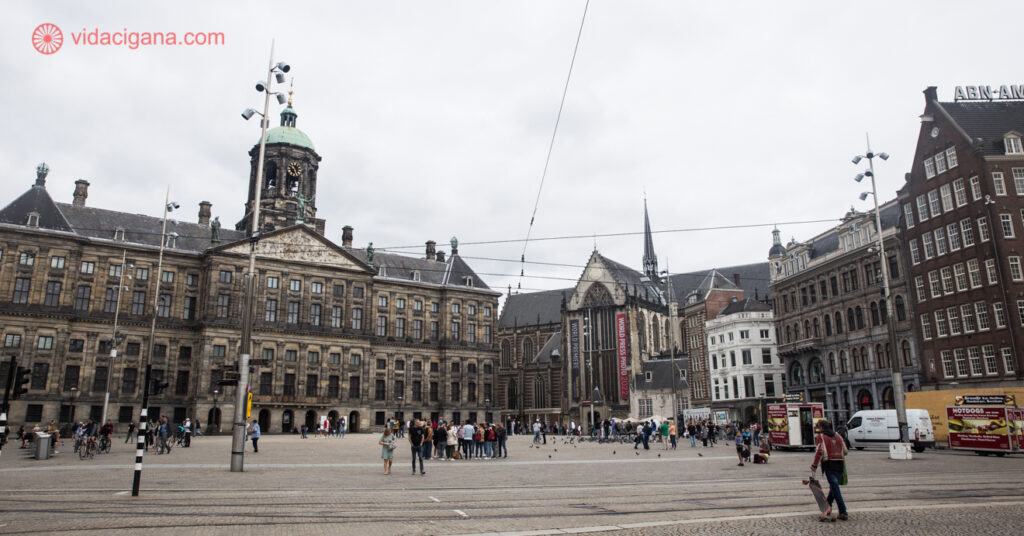 No cenáro da Praça Dam, turistas apreciam as edificações ao seu redor. Entre elas estão o Koninklijk Paleis e a Nieuwe Kerk.