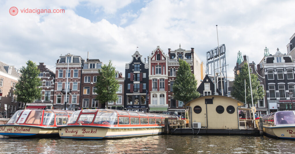Na imagem, o cenário de Amsterdã: construções típicas ao fundo, e barcos estacionados no píer de um dos canais da cidade. 