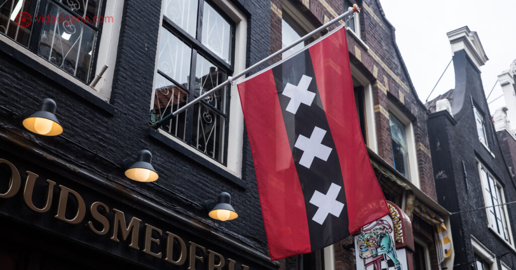 A imagem mostra a bandeira de Amsterdam hasteada na fachada de um estabelecimento.
