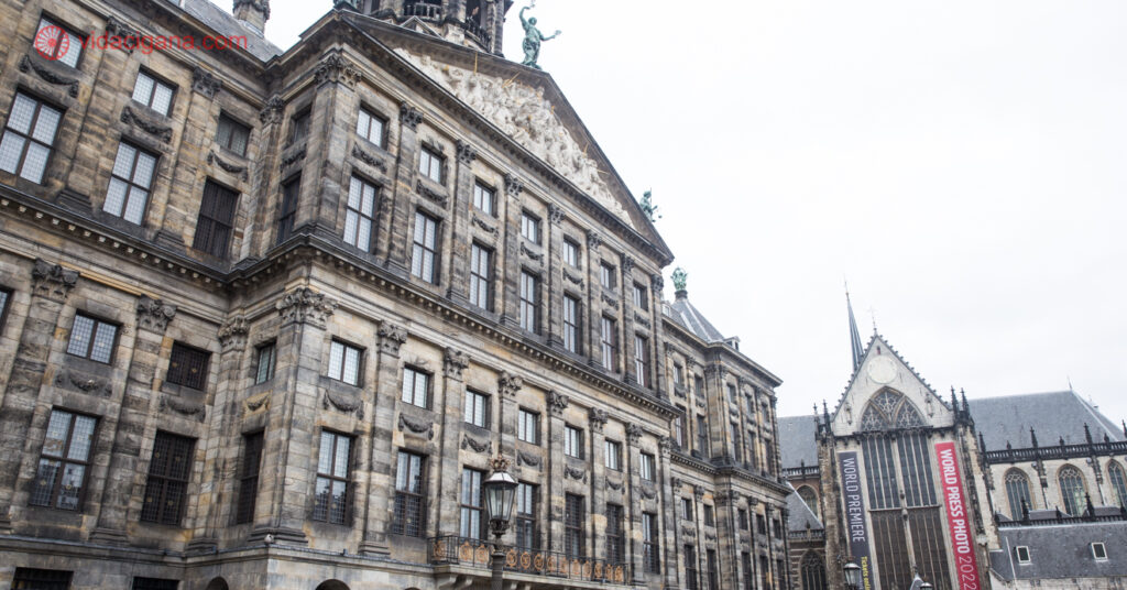 A imagem mostra a fachada do Koninklijk Paleis, o antigo Palácio Real. Ao lado, é possível ver a Igreja Nova. 