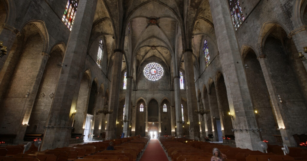 O interior da Santa Maria del Mar tem estilo gótico catalão. Na imagem vemos os bancos, o caminho do altar até a porta e detalhes ornamentais da construção.