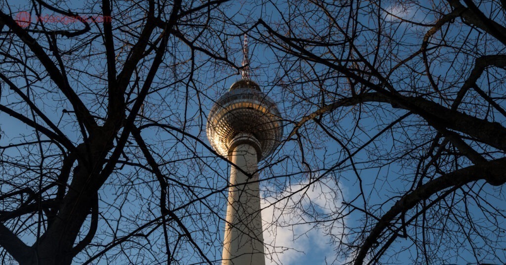 O topo da Torre de Televisão de Berlim mesclada entre galhos de árvores. 