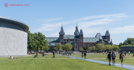 A Museumplein Amsterdam, com o Rijksmuseum ao fundo e o Museu Van Gogh do lado esquerdo. Um grande gramado é visto