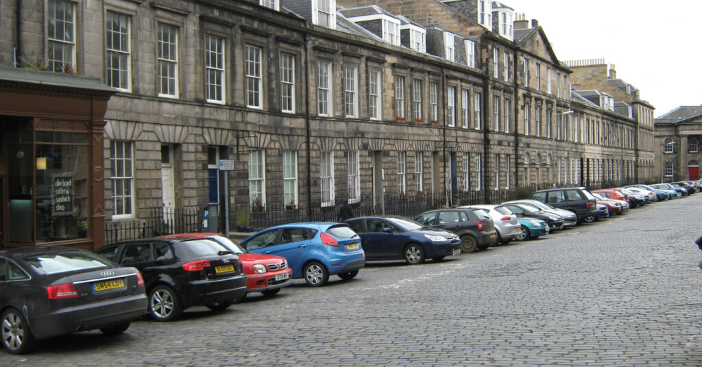 Carros estacionados em frente aos prédios tradicionais do bairro de Broughton, em uma rua de paralelepípedos. 