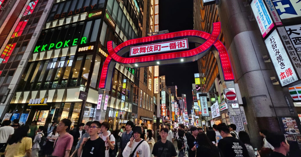 Rua do bairro de Kabukicho, local de entretenimento, com letreiros diversos e pessoas transitando. 