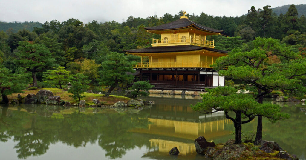 O templo zen Kinkaku-ji, uma construção amarela em meio a um lago e árvores. 