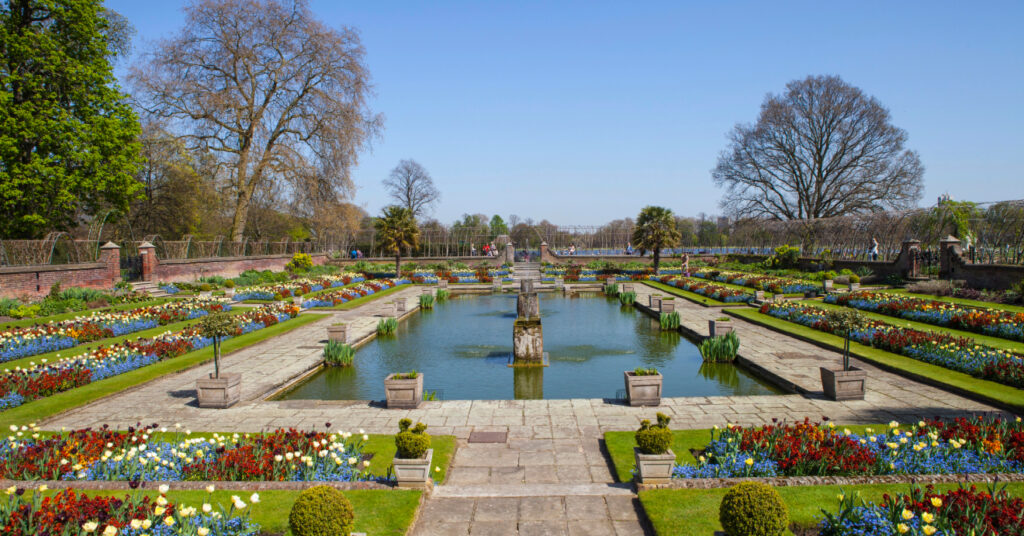 Jardim florido e bem-cuidado ao redor de fonte e espelho d'água no Kensington Gardens.