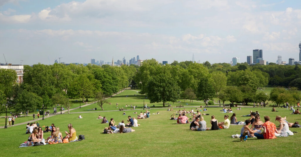 Pessoas sentadas no gramado da colina Primrose Hill em um dia de sol. 